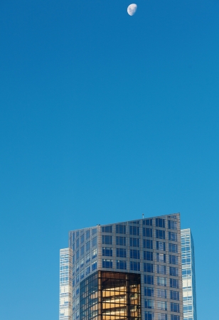 Beautiful modern office buildings and the moon against the blue skyの写真素材