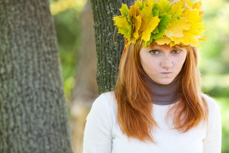 portrait of a beautiful young redhead teenager woman in a wreath of maple leavesの写真素材