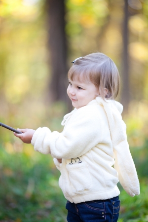 beautiful little girl with a stick on the autumn forestの写真素材
