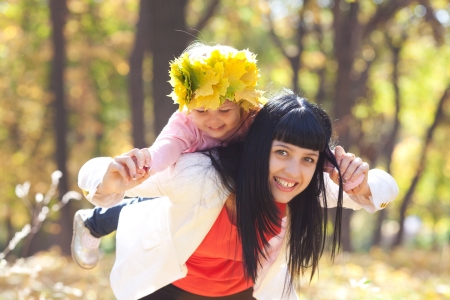 beautiful young mother holding her daughter in a wreath of maple leaves on backの写真素材