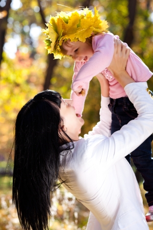 beautiful young mother holding her daughter in a wreath of maple leaves の写真素材