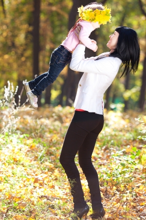 beautiful young mother holding her daughter in a wreath of maple leaves の写真素材