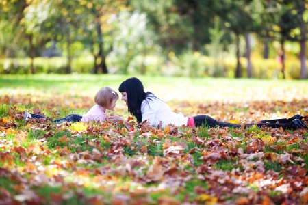 beautiful young mother and her daughter lying on the autumn leavesの写真素材