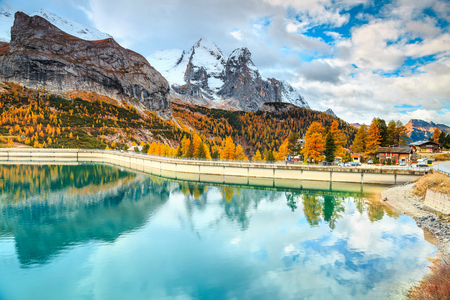 Amazing autumn landscape, alpine lake and yellow pine trees, Fedaia lake with famous Marmolada peak in background, Dolomites, Italy, Europeの写真素材