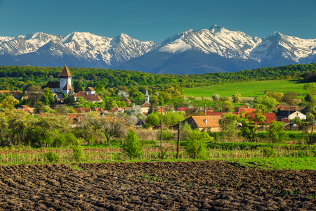Breathtaking spring countryside landscape, church of Hosman and high snowy Fagaras mountains in background, Sibiu region, Transylvania, Romania, Europeの写真素材