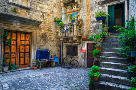 Beautiful narrow street with stone houses. Old stone houses and entrances decorated with flowers. Cozy apartments and paved street with flowery entrances, Trogir, Dalmatia, Croatia, Europeの写真素材