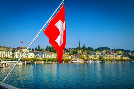 Popular travel place in Lucerne with famous buildings and Reuss river. Waving Swiss flag on the...