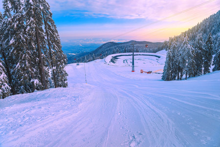 Fabulous snow covered pine trees and winter ski resort with colorful ski gondolas at sunrise. Ski...