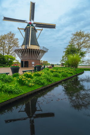 Cute wooden windmill on the flowery waterfront in the stunning Keukenhof garden, Lisse, Netherlands,...