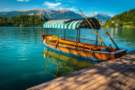 Traditional touristic wooden rowing Pletna boat anchored at the pier. Wooden Pletna boat on the famous Bled lake and medieval castle on the hill in background, Slovenia, Europeの写真素材