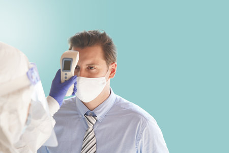 Disease control experts  use an Infrared thermometer equipment to check the temperature on the forehead and use alcohol gel to screen the patients addicted to Covid before entering the building.の写真素材