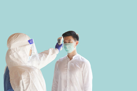 Disease control experts  use an Infrared thermometer equipment to check the temperature on the forehead and use alcohol gel to screen the patients addicted to Covid before entering the building.の写真素材