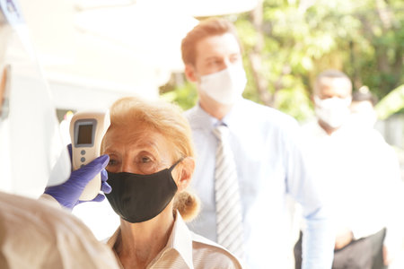 Disease control experts  use an Infrared thermometer equipment to check the temperature on the forehead and use alcohol gel to screen the patients addicted to Covid before entering the building.の写真素材