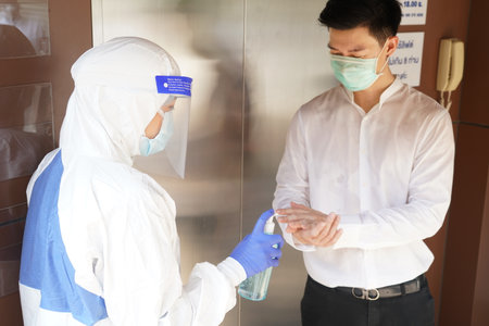 Disease control experts  use an Infrared thermometer equipment to check the temperature on the forehead and use alcohol gel to screen the patients addicted to Covid before entering the building.の写真素材