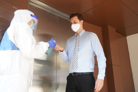 Disease control experts  use an Infrared thermometer equipment to check the temperature on the forehead and use alcohol gel to screen the patients addicted to Covid before entering the building.の写真素材
