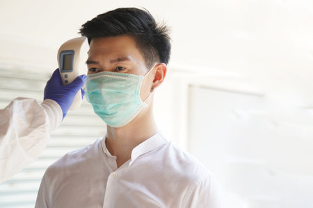 Disease control experts  use an Infrared thermometer equipment to check the temperature on the forehead and use alcohol gel to screen the patients addicted to before entering the building.の写真素材