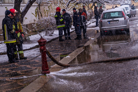 Uzhgorod, Ukraine - December 1, 2016: Firefighters stand near flowing worthless old hydrant during fire extinguishing on a city street.のeditorial素材