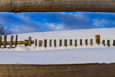 Wooden fence in the snow at the edge of a mountain village in the Carpathian Mountains.の写真素材