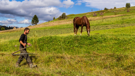 Pylypets, Ukraine - September 15, 2017: Local farmer mowing grass on a mountain meadow in the Carpathians on a beautiful sunny morning in early autumn.のeditorial素材