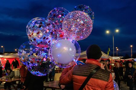 Uzhgorod, Ukraine - February 16, 2020: A man holds colorful balloons with LED backlight during a traditional winter festival.のeditorial素材
