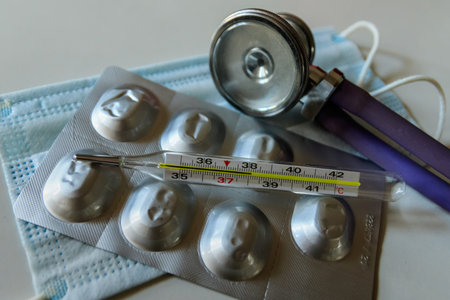 Mercury thermometer shows high temperature on the background of the face mask, pills in blister pack...