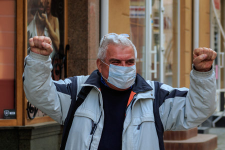 Uzhgorod, Ukraine - March 18, 2020: A man in a medical mask in the city center calls for optimism...