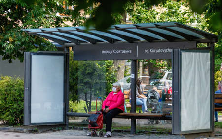 Uzhgorod, Ukraine - June 3, 2020: Elderly woman in a protective mask waiting for a bus at the bus stop. COVID-19 disease protection.のeditorial素材