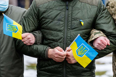 Uzhhorod, Ukraine - February 16, 2022: Officers in protective masks with flags of Ukraine and civilians united in the Live Chain during the celebration of the National Unity Day.のeditorial素材