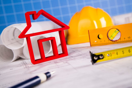 House under construction, blueprints and helmet