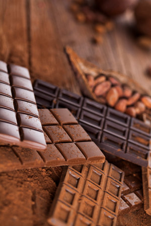 Chocolate bar, candy sweet, cacao beans and powder on wooden background