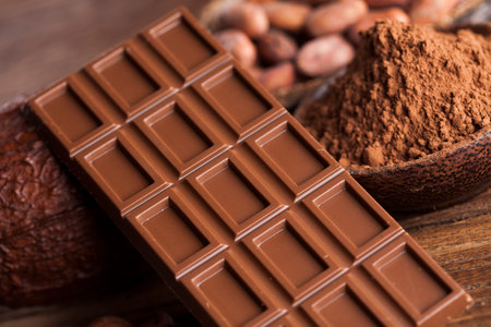 Chocolate bar, candy sweet, cacao beans and powder on wooden background