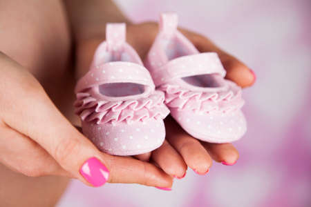Pregnant woman holding baby shoes in her handsの写真素材
