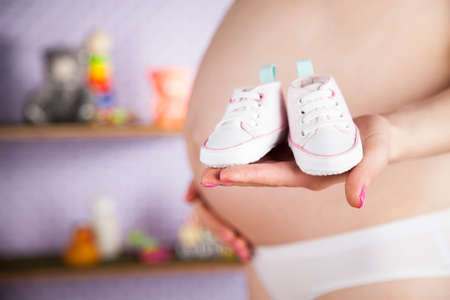 Pregnant woman holding baby shoes in her handsの写真素材