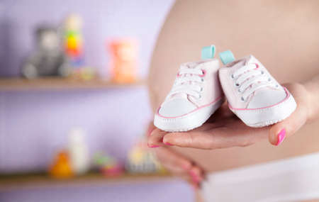 Pregnant woman holding baby shoes in her handsの写真素材