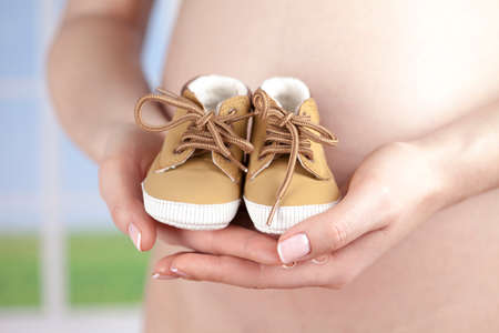 Pregnant woman holding baby shoes in her handsの写真素材