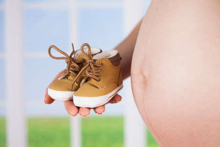 Pregnant woman holding baby shoes in her handsの写真素材