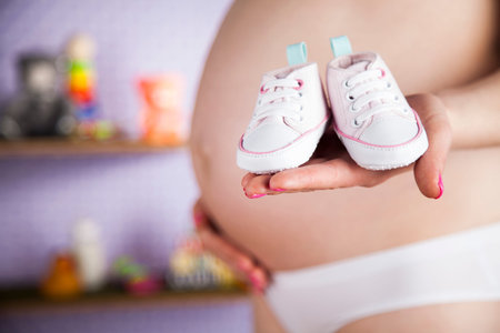Pregnant woman holding baby shoes in her handsの写真素材