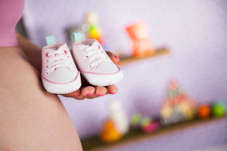 Pregnant woman holding baby shoes in her handsの写真素材