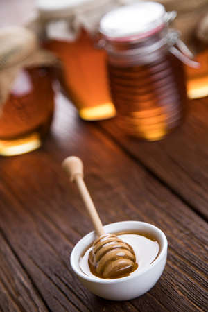 Honey in jar with honey dipper on wooden backgroundの写真素材