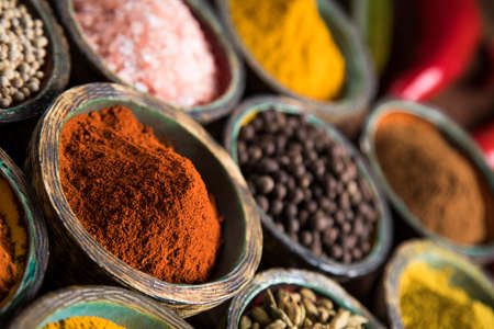 A selection of various colorful spices on a wooden table in bowlsの写真素材