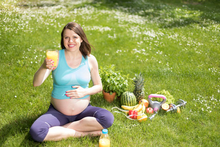 Pregnant woman doing fitness exercise on the grass