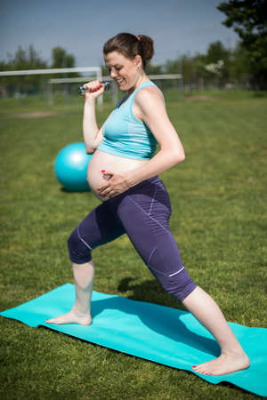 Pregnant woman doing fitness exercise on the grassの写真素材