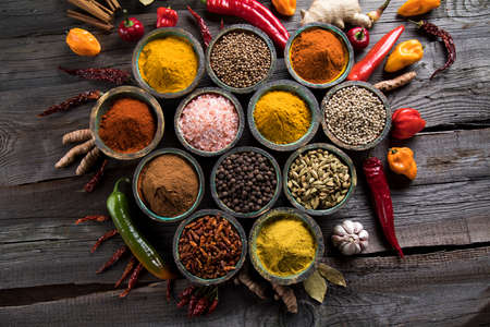 A selection of various colorful spices on a wooden table in bowlsの写真素材