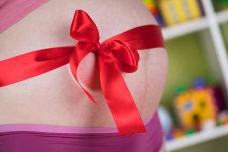 Pregnant woman belly with red ribbon giftの写真素材