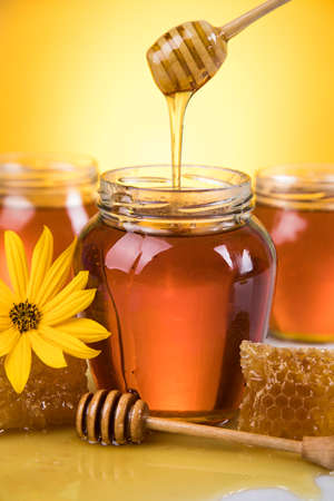 Honey dripping from a wooden honey dipper in a jarの写真素材
