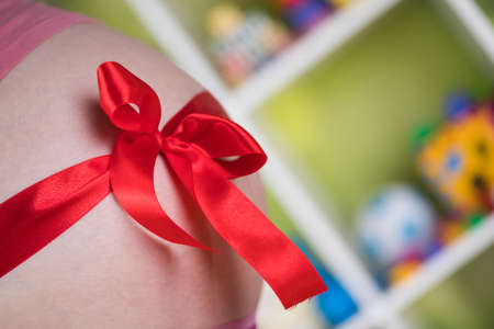 Pregnant woman belly with red ribbon giftの写真素材