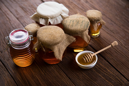 Honey dripping from a wooden honey dipper in a jar on wooden background