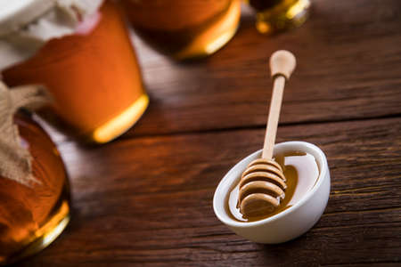 Honey in jar with honey dipper on wooden backgroundの写真素材