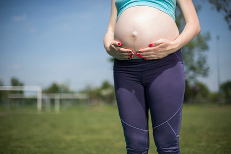 Pregnant woman doing fitness exercise on the grass