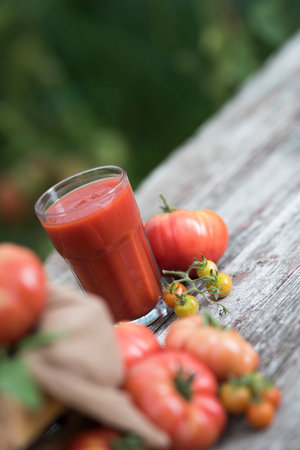 Tomato juice in glass and fresh tomatoes on wooden table in gardenの写真素材